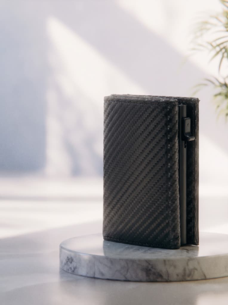 Front view of Elzinore's slim carbon fiber wallet standing on a marble pedestal